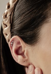 Pendiente de oreja de plata con diseño de estrella, adornado con pequeñas piedras preciosas. Colocado sobre cabello oscuro con una diadema de satén beige. Enfoque en primer plano en la oreja.