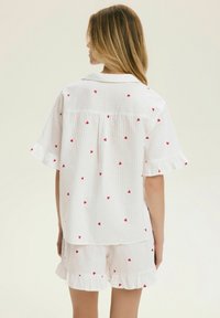 Białe bawełniane piżamy w czerwone wzory serc, z falbaniastymi krótkimi rękawami i szortami, o prążkowanej fakturze i luźnym kroju.