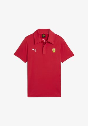 Červená polo košeľa má logo Puma na ľavej hrudi a emblém Ferrari nad ľavou stranou lemu, s klasickým dizajnom goliera.