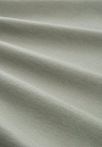 Jasnozielona tkanina o gładkiej fakturze, z delikatnymi zmarszczkami i fałdami, przedstawiająca prosty wzór bez wzorów ani akcentów.