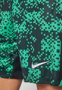 Grün und schwarz gemusterte Sportshorts mit einem pixelierten Design, aus leichtem Material gefertigt, mit einem kleinen weißen Nike-Logo an der Seite.