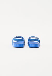 Blå gummisandaler med breda remmar och strukturerad fotbädd, med platt sula och minimalistisk design.