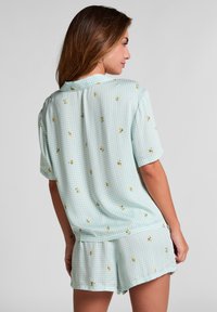Kortärmad pyjamasset i ljusblått gingham med gula blommönster. Mjukt tyg, avslappnad passform, med shorts och krage.