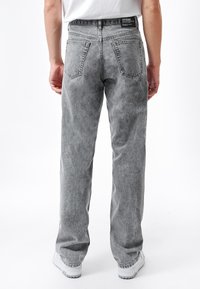 Jeans in denim grigio con una vestibilità comoda, tasche posteriori visibili e una texture leggermente sbiadita. Il cinturino presenta un'etichetta del marchio.