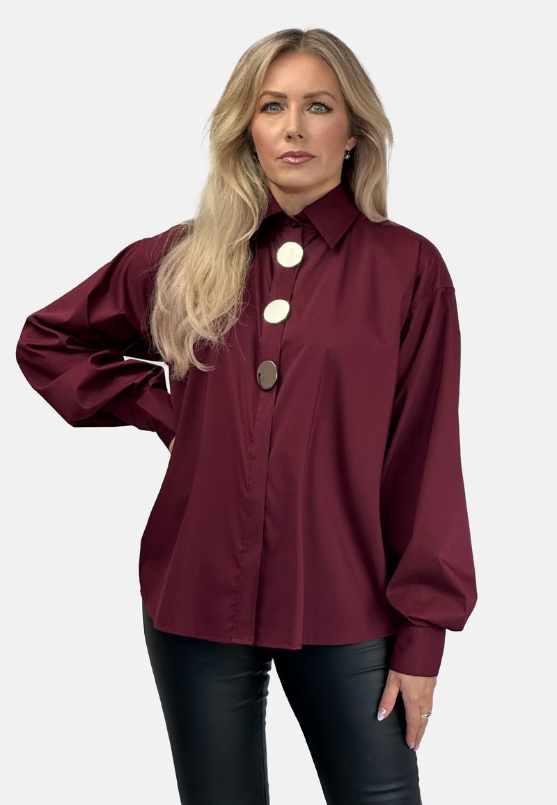 Bordowa koszula z guzikami i wysokim kołnierzem, z trzema dużymi srebrnymi guzikami oraz luźnymi rękawami. Zestawiona z dopasowanymi czarnymi spodniami.