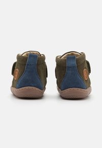 Dois sapatos a altura do tornozelo; camurça verde-oliva com detalhes em camurça azul. Biqueira arredondada, tira de velcro e solado de borracha com aderência texturizada.