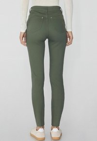 Jean skinny vert olive taille haute, avec poches arrière et passants de ceinture latéraux, associés à des baskets claires.