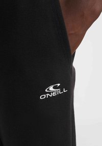 Schwarze Jogginghose aus Stoff mit gerippter Textur, mit einem weißen gestickten O'Neill-Logo am linken Bein. Nahaufnahme der Nähdetails.