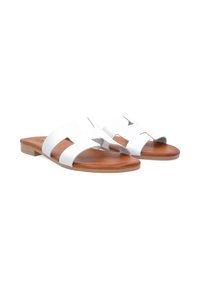 White leather slide sandals featuring an open toe, cutout design, brown sole, and flat heel for comfort.