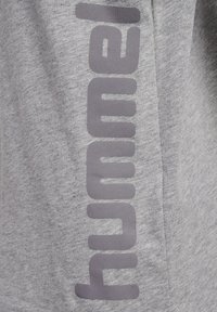 Grå T-shirt i bomull med en framträdande vertikal logotyp i mörkgrått. Tyget har en slät textur med subtila variationer.