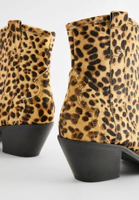 Kotníkové boty s leopardím potiskem a texturovaným, kožešinovým povrchem, s nízkým černým podpatkem a podrobným prošíváním po stranách.