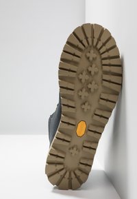 Sort vandrestøvlesål med dybe profiler og et gult Vibram-logo. Tekstureret gummi for greb og stabilitet på varieret terræn.