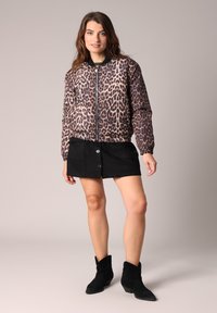 Jasje met luipaardprint en rits aan de voorkant, elastische manchetten en zoom; gecombineerd met een zwarte suède mini-jurk en zwarte enkellaarsjes.