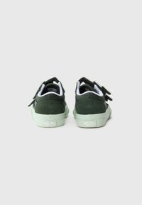 Une paire de baskets basses Vans vert foncé avec des semelles vert clair, vue de l'arrière sur un fond blanc uni.