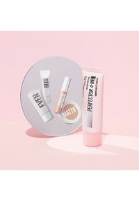 Set di quattro cosmetici Maybelline: tubetti bianchi e rosa etichettati "Blur", "Even", "Mattify" e un tubetto rosa di "Perfector 4-in-1", disposti attorno a uno specchio circolare.
