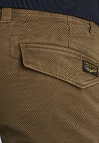 Bruine textuur broek met een kenmerkende achterzak en een PME Legend label. De stof heeft een subtiel patroon en zichtbare stikseldetails.