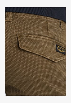 Braune Textilhose mit einer markanten Gesäßtasche und einem PME Legend Aufnäher. Der Stoff hat ein dezentes Muster und sichtbare Nahtdetails.