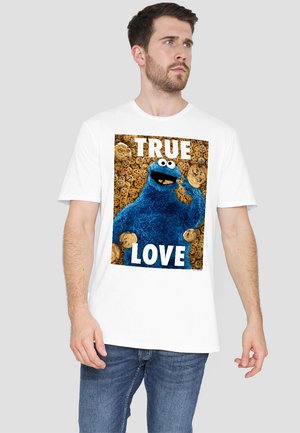 Weißes Baumwoll-T-Shirt mit einem grafischen Motiv eines blauen Charakters, der Kekse hält, mit dem Text "WAHRE LIEBE" über einem Keks-Hintergrund.