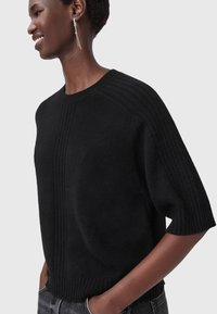 Maglione nero a maniche corte realizzato in morbido tessuto a maglia, caratterizzato da dettagli a coste e una vestibilità rilassata. Leggera texture lungo le cuciture.