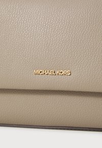 Beige strukturiertes Leder-Clutch mit goldfarbenem "Michael Kors"-Logo. Verfügt über ein gefaltetes Design und eine elegante Oberfläche, die Einfachheit und Eleganz betont.