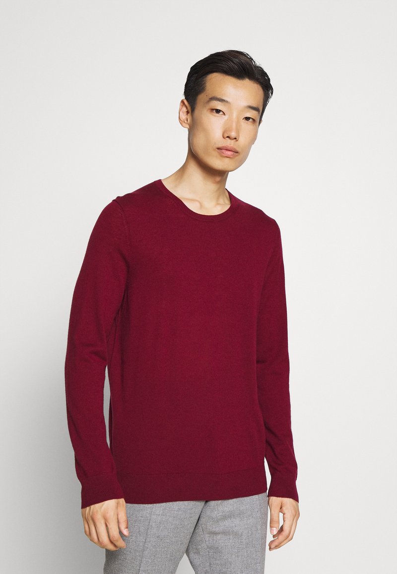 Burgunderfarbener Strickpullover mit Rundhalsausschnitt und langen Ärmeln, der eine glatte Textur sowie gerippte Bündchen und Saum aufweist.