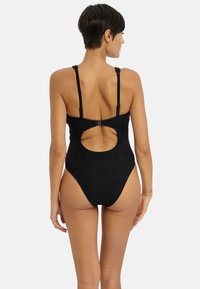Maillot de bain une pièce noir avec des bretelles réglables et une découpe en cœur au dos. Le tissu texturé renforce l'intérêt visuel.