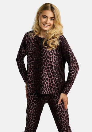 Blondínka sa usmieva, má na sebe zladený dlhý rukáv a nohavice s tmavofialovým a ružovým leopardím vzorom.