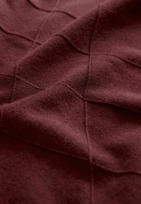 Burgundiškai raštuota megzto audinio medžiaga su tekstūruota deimanto forma, matomomis siūlių detalėmis ir švelnia, lygiomis tekstūra.
