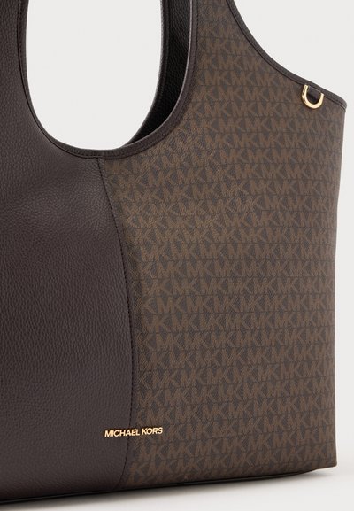 Gros plan sur un sac cabas marron Michael Kors, avec un empiècement en cuir grainé foncé, un motif monogramme répétitif et des pièces métalliques dorées.