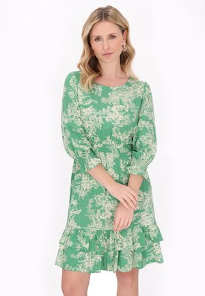 Grünes Blumenmusterkleid mit Dreiviertelärmeln, rüschendem Saum, elastischem Bund und weißen botanischen Mustern auf einem einfarbigen Hintergrund.