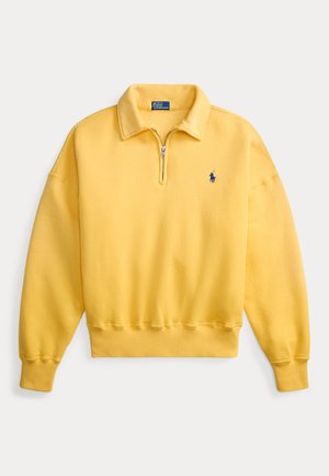 Gul genser med glidelås i halsen laget av bomullsblanding, med ribbestrikkede mansjetter og kant, og en liten blå logo på venstre bryst. Myk tekstur.