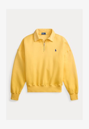 Sudadera amarilla con cremallera en el cuello, confeccionada con una mezcla de algodón, con puños y dobladillo acanalados, y un pequeño logo azul en el pecho izquierdo. Textura suave.