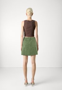 Top corto marrone in cotone e gonna A-line in corduroy verde con tasche frontali, abbinata a sandali trasparenti con tacco. Texture morbide.