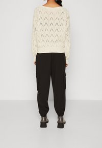 Krämfärgad stickad tröja med en texturerad chevronmönster, ihopparad med svarta cargobyxor med sidofickor och elastiska muddarmar.