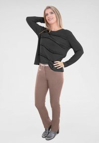 Schwarzes Langarm-Oberteil mit wellenförmigem Texturmuster; kombiniert mit schlanken, hellbraunen Hosen und schwarzen Absatzstiefeln bis zum Knöchel.