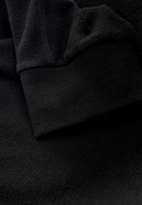 Tifă neagră cu o textură nervată aproape de manșetă, având o zonă netedă și moale. Materialul este ușor și se întinde ușor.