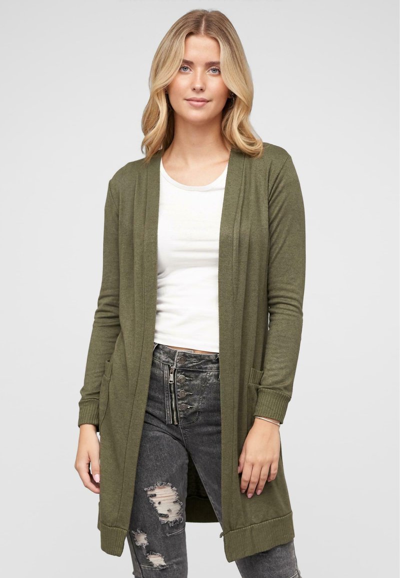 Oliivinvihreä neulecardigan, jossa on avoin etuosa, pitkät hihat, ribbireunukset ja sivutaskut, yhdistetty valkoisen paidan ja kulutettujen tummien farkkujen kanssa.