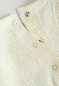 Tissu crème avec une texture froissée. Présente deux boutons-pression : un argenté et un beige assorti.