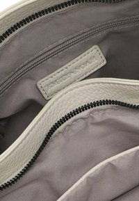 Leather bag interior with gray fabric lining, featuring two zippered compartments and a subtle label tag in light gray.