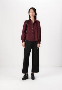Burgundy long-sleeve shirt with button-up front and textured fabric, paired with black wide-leg trousers and black chunky loafers.