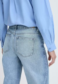 Šviesiai mėlyna marškinėlių su ilgomis rankovėmis palaidinė, derinama su išblukusiomis mėlynomis džinsomis, turinčiomis dvigubus užpakalinius kišenės ir tiesiu sijonu.