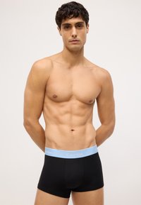 Čierne boxerky s ľahko modrým pásom, na ktorom je logo "Calvin Klein". Tkanina vyzerá hladko a elasticky.