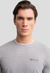 Camiseta gris con una fina textura a rayas, que presenta un cuello redondo blanco en contraste y un pequeño logo bordado en el pecho.