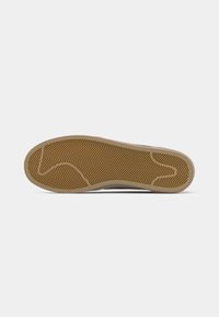Shoe sole with brown rubber tread in chevron pattern and curved grooves, shown flat against a white background.