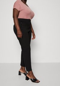 Pantalons tailleur noirs à taille haute et poches latérales, associés à un haut rose à manches courtes. Des sandales noires à talons hauts complètent le look.