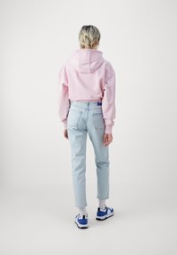 Sudadera rosa recortada; vaqueros azul claro; calcetines blancos; zapatillas azules y negras; costuras y bolsillos visibles; fondo liso.