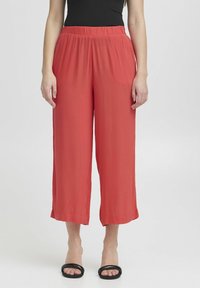 Rote weit geschnittene Hose mit elastischem Bund, aus leichtem Stoff gefertigt. Sie zeichnet sich durch einen lässigen Schnitt und einen geraden Saum aus. Kombiniert mit schwarzen Sandalen.