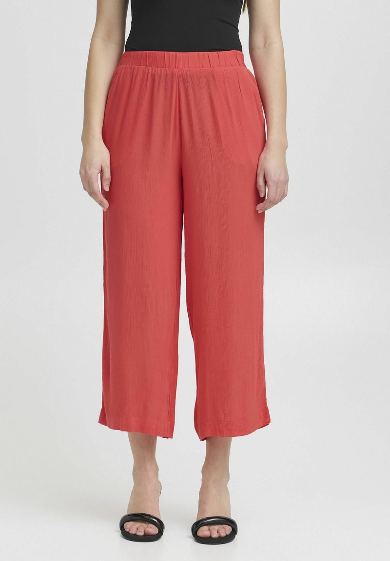 Rote weit geschnittene Hose mit elastischem Bund, aus leichtem Stoff gefertigt. Sie zeichnet sich durch einen lässigen Schnitt und einen geraden Saum aus. Kombiniert mit schwarzen Sandalen.
