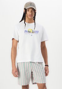 Hvit bomulls t-skjorte med en blå logo og en gul sitrongrafikk. Sammen med rosa og grønne stripete shorts i et lett stoff.