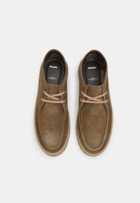 Bruine suède schoenen met een ronde neus, twee-kleurige veters en een gestructureerde zool. De binnenkant heeft een zwarte voering met het merklogo.